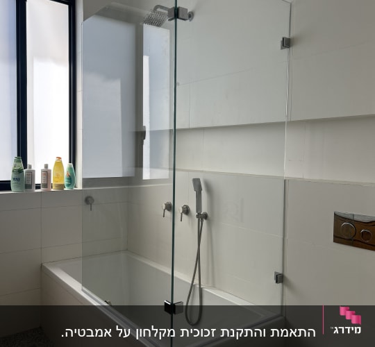 מקלחת עם דלת זכוכית, ראש מקלחת ומוצרים על אדן החלון